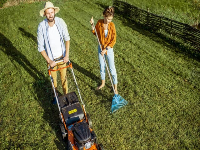 Man and woman mowing and raking their yard.